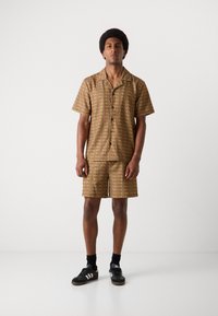 Short-sleeve shirt and shorts set in brown with a repeating pattern. Made of lightweight fabric, featuring a button-up front and relaxed fit.