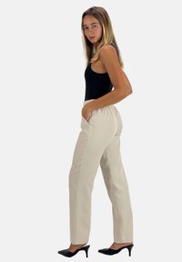 Beige, high-waisted broek met een gladde textuur en zijzakken, gecombineerd met een zwart mouwloos topje en zwarte hoge hakken.