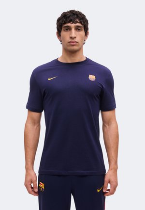 Homme portant un t-shirt Nike FC Barcelone bleu marine et un short assorti, debout devant un fond uni clair.