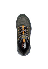 Zapatilla deportiva de malla verde con detalles en naranja, cordones grises, punta redondeada, collar acolchado y una suela negra gruesa con agarre texturizado.