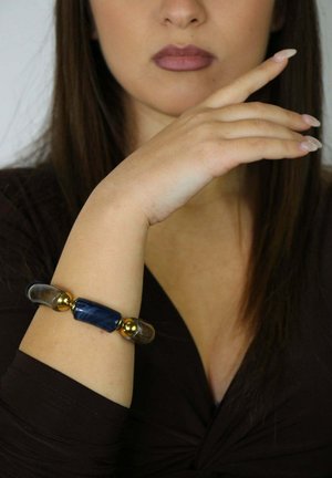 Perline blu e trasparenti con accenti dorati formano un braccialetto su un polso, mostrando una texture liscia e una forma allungata e ovale.