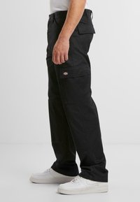 Svarta cargo-byxor i slitstarkt material, med flera fickor, en avslappnad passform och en patch-logotyp på sidan.