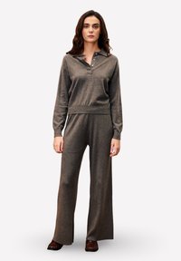 Ensemble de vêtements de détente gris en tricot comprenant un haut à col et à boutons, ainsi que des pantalons à jambes larges. Le tissu a une texture douce et une coupe décontractée.