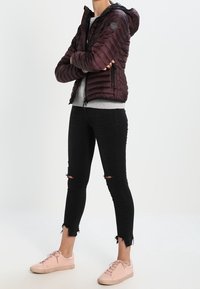 Chaqueta acolchada burdeos con capucha, textura acolchada, combinada con jeans skinny negros desgastados y zapatillas bajas rosa claro.