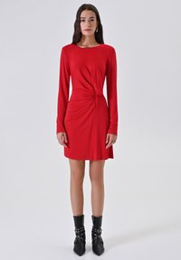 Rode lange mouwen jurk met een knoopdetail aan de zijkant, gladde stof en een ronde halslijn. Draagt zwarte enkellaarsjes met zilveren accenten.