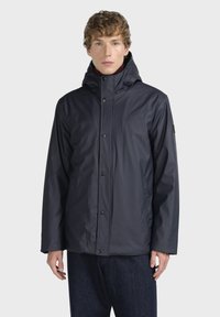 Námořnická modrá voděodoln á bunda s vysokým límcem, zapínáním na patentky a dlouhými rukávy. Vyrobeno z hladkého, lehkého materiálu.