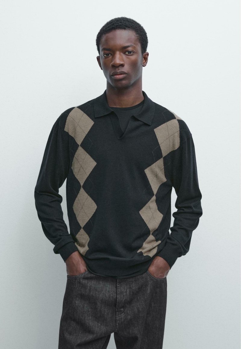 Zwarte trui met lange mouwen, beige ruitpatronen, een kraag en een textuurrijke stof. Model draagt donkergrijze broek.