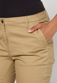 Beige cotton pants featuring side pockets, a classic fit, and a smooth texture. Includes a front button closure and belt loops.