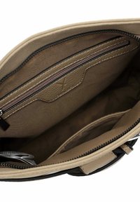 Vue intérieure d'un sac à main beige montrant la doublure en tissu, une poche zippée, un compartiment ouvert et une petite étiquette pliée à l'intérieur.