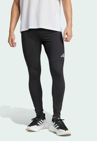 Leggings atléticos negros hechos de un material elástico con un diseño ajustado, que presentan costuras horizontales y un acento de logo en el muslo.