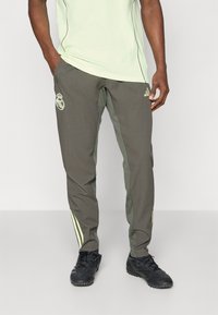 Olive green athletic pants with stretchy material, featuring light green stripes on the sides and a logo on the left thigh. Designed for comfort.