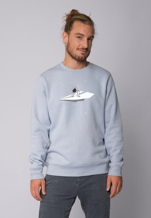 Lichtblauwe sweatshirt gemaakt van zachte stof. Voorzien van een afbeelding van een astronaut op een papieren vliegtuigje, tegen een sterrenachtergrond.