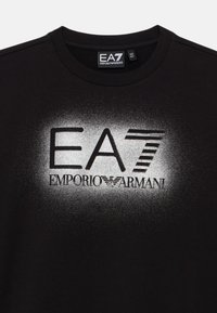 Črna bombažna majica s okroglim izrezom in obliko logotipa v srebrni prelivajoči se barvi: »EA7 Emporio Armani« z črtastimi poudarki zgoraj.
