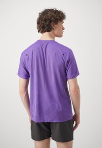 Lila Sport-T-Shirt mit einem atmungsaktiven Mesh-Muster, kurzen Ärmeln und kleinen schwarzen Akzenten an den Schultern.