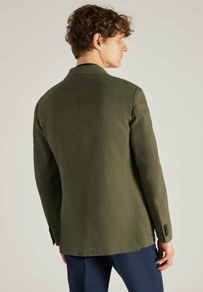 Blazer vert olive avec une coupe ajustée, des épaules structurées et deux boutons. Dispose d'un tissu texturé et d'une fente au dos.
