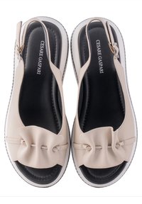 Sandales en cuir beige avec un bout rond, design slip-on et détail de nœud décoratif. Semelles intérieures noires et semelles extérieures blanches. Bride de talon ajustable.