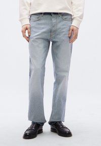 Τζιν παντελόνια από ανοιχτό μπλε τζιν με ίσια γραμμή, σχέδιο πέντε τσεπών και διακριτική ξεθωριασμένη υφή. Φορεμένα με μαύρα παπούτσια χωρίς κορδόνια και ανοιχτόχρωμο φούτερ.