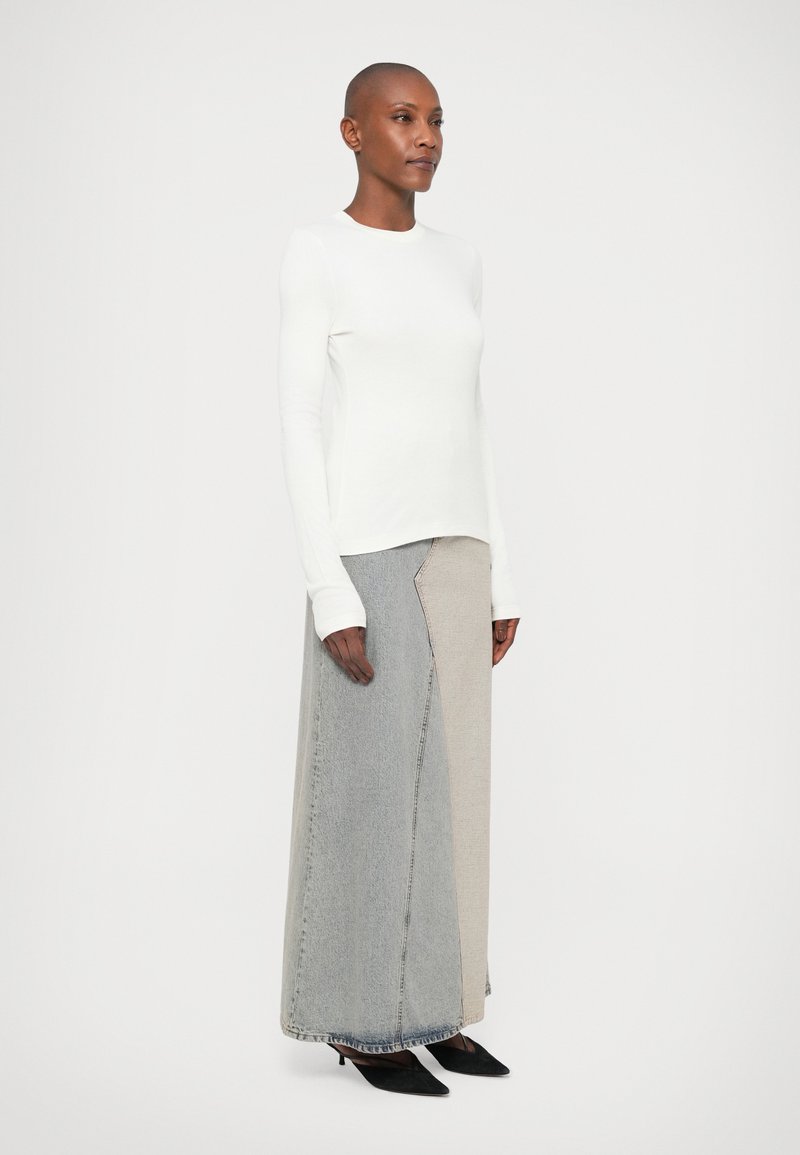 White long-sleeve top paired with a patchwork maxi skirt featuring grey and beige denim sections. Model wears black pointed heels.