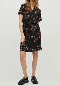 Sort kortærmet kjole med blomstermønster i pink og grøn, med knaplukning foran og bindebånd i taljen, kombineret med sorte platformsko.