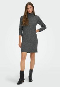 Robe en maille grise à col roulé avec des manches longues et une silhouette ajustée, se terminant au-dessus du genou. Associée à des bottes noires à la cheville.