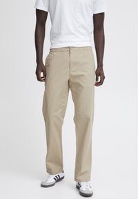 Pantaloni beige a gamba dritta con chiusura a bottone e tasche laterali. Indossati con una t-shirt bianca semplice e scarpe da ginnastica bianche a strisce nere.