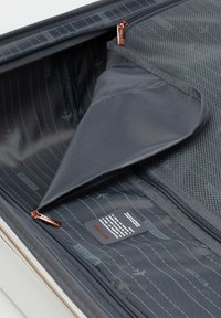 Interno di una valigia grigia con scomparti con zip. Il rivestimento testurizzato presenta pattern di aeroplani. Include un'etichetta di cura dettagliata e chiusura a zip.