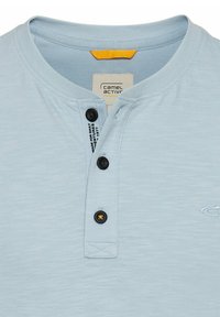 Lyseblå bomulds t-shirt med korte ærmer, der har en henley-udskæring med tre sorte knapper og et lille logo på brystet. Struktureret stof.