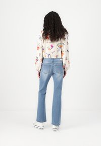 Light blue flared jeans with a high waist and two back pockets, paired with a floral patterned blouse featuring billowy sleeves.