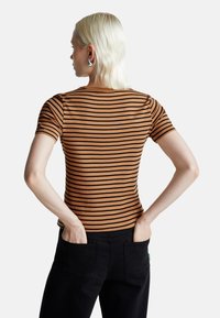 Krótki rękaw t-shirt w brązowo-czarne paski, dopasowany krój, wykonany z bawełny, gładka tekstura, noszony z czarnymi dżinsami, widok z tyłu.