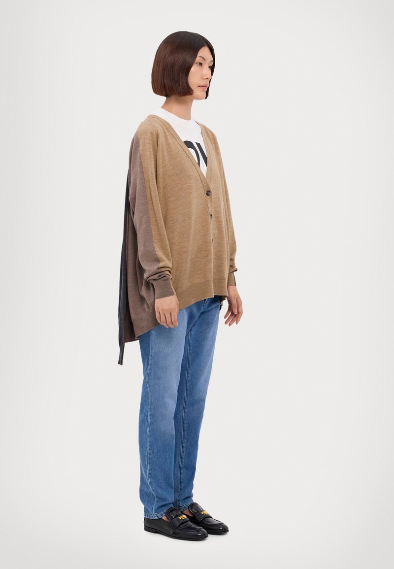Cardigan marrone con gradiente, maniche lunghe, bottoni davanti e retro più lungo. Abbinato a jeans azzurri chiari e mocassini neri.
