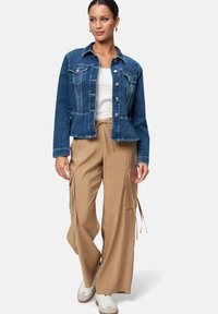 Jeansjack met knoopsluiting, twee borstzakken, blauwe kleur; gecombineerd met losse beige cargo broek met zijzakken en een trekkoord.