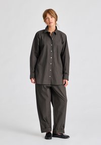 Camicia button-up grigia scura con taschino, abbinata a pantaloni larghi grigi scuri. Il modello indossa ciabatte nere. Vestito casual.