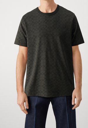 Musta lyhythihainen t-paita, jossa on teksturoitu pyöreä kuvio, pyöreä pääntie ja rento-istuvuus. Yhdistetty tummaan farkkuhousuun.