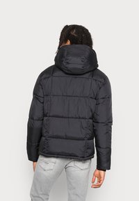 Černá prošívaná bunda s kapucí, s prošívaným vzorem a hladkou texturou. Design má elastické manžety a mírně zkrácený spodní lem.