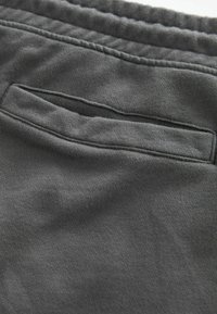 Grauer Stoff, weiche Textur, mit einer Rückentasche und genähten Details entlang des Bunds, zeigt glattes, leichtes Material.