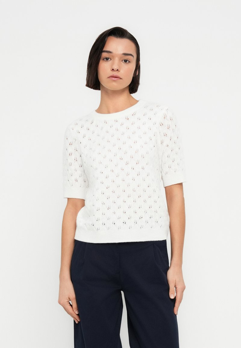 Λευκό πλεκτό πουλόβερ με κοντά μανίκια, με μοτίβο ρόμβου και υφή. Συνδυάζεται με παντελόνι σε σκούρο ναυτικό μπλε χρώμα.