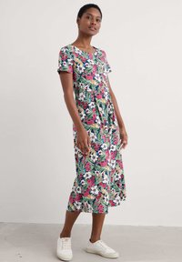 Cvetna obleka s temno modrim ozadjem in rožami v roza in rumeni barvi, kratkimi rokavi in dolžino do sredine meč, v kombinaciji z belimi športnimi copati.