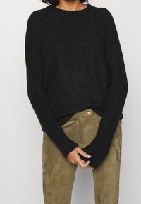 Pull noir et duveteux à manches longues et col rond, associé à un pantalon en daim vert olive avec fermeture à boutons à l'avant.