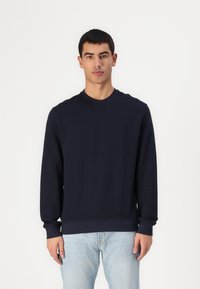 Sudadera de manga larga en mezcla de algodón de color marino, con cuello redondo acanalado y puños acanalados, y un dobladillo recto. Combinada con jeans de un azul claro.