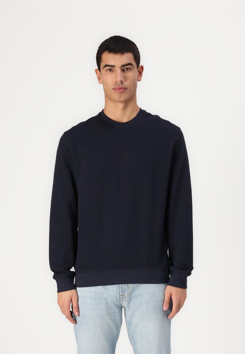 Sudadera de manga larga en mezcla de algodón de color marino, con cuello redondo acanalado y puños acanalados, y un dobladillo recto. Combinada con jeans de un azul claro.