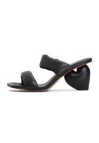 Sandali in pelle nera a scivolo con tacco a forma di cuore. Presentano due cinturini larghi e una superficie liscia e strutturata. Suola in gomma resistente.