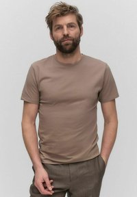 T-shirt z krótkim rękawem, okrągłym dekoltem w jasnobrązowym kolorze z bawełny, z gładką teksturą i dopasowanym krojem. W zestawie z brązowymi spodniami.
