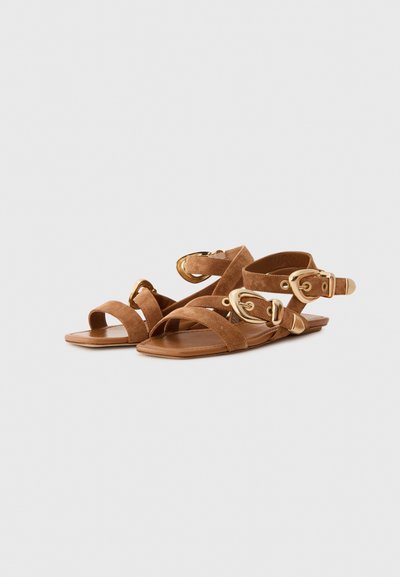 Bruna mockaskinnsandaler med flera korskorsande remmar och detaljer i guldton. Platt sula, öppen tå-design och justerbara spännen.
