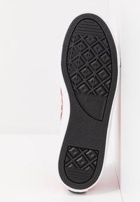 Semelle en caoutchouc noire d'une chaussure Converse All Star rouge et blanche montrant le motif de la bande de roulement texturé et le logo de la marque.