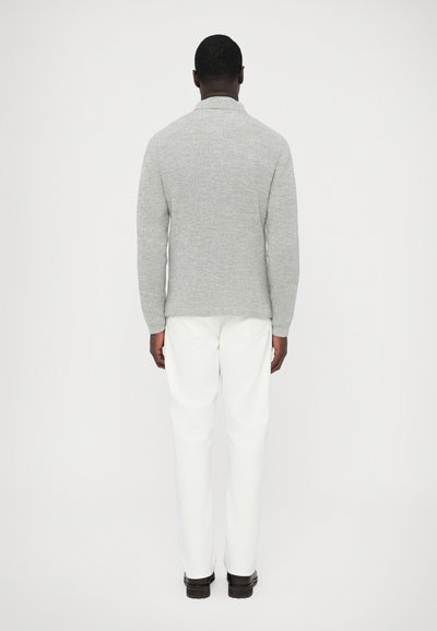 Pilkas megztas megztinis su apykakle, prigludusiu siluetu ir briaunuota tekstūra, derinamas su baltais kelnėmis ir tamsiais batais. Paprastas ir modernus dizainas.