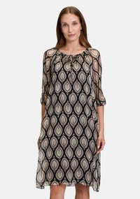 Schwarz-beige gemustertes Kleid mit rundem Ausschnitt und einem Bindedetail. Dreiviertelärmel, durchsichtiger Stoff und eine lockere Passform.