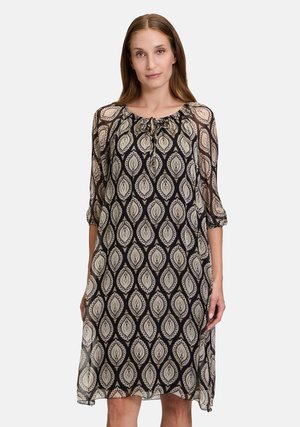 Black and beige patterned dress with a round neckline and a tie detail. Three-quarter sleeves, sheer fabric, and a loose fit.