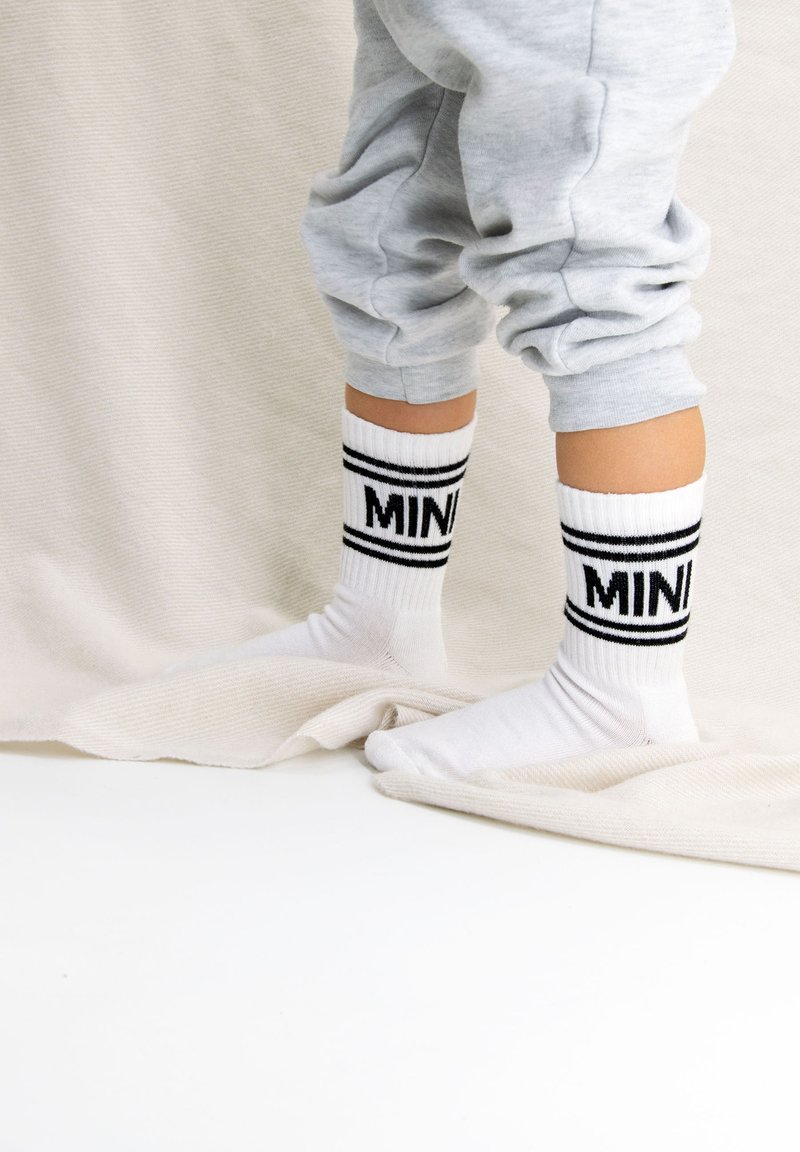 Weiße Baumwollsocken mit schwarzen Streifen und "MINI"-Text; getragen mit grauen Jogginghosen, die eine gerippte Textur und weichen Stoff aufweisen.