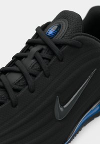 Μαύρο αθλητικό παπούτσι με υφή στο επάνω μέρος, στρογγυλά κορδόνια και γυαλιστερή επιγραφή Nike swoosh. Μπλε λεπτομέρειες στη σόλα.