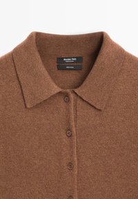 Maglione di lana marrone con design colletto, caratterizzato da una chiusura frontale con bottoni e maglia testurizzata. Etichette indicano marca e materiale.